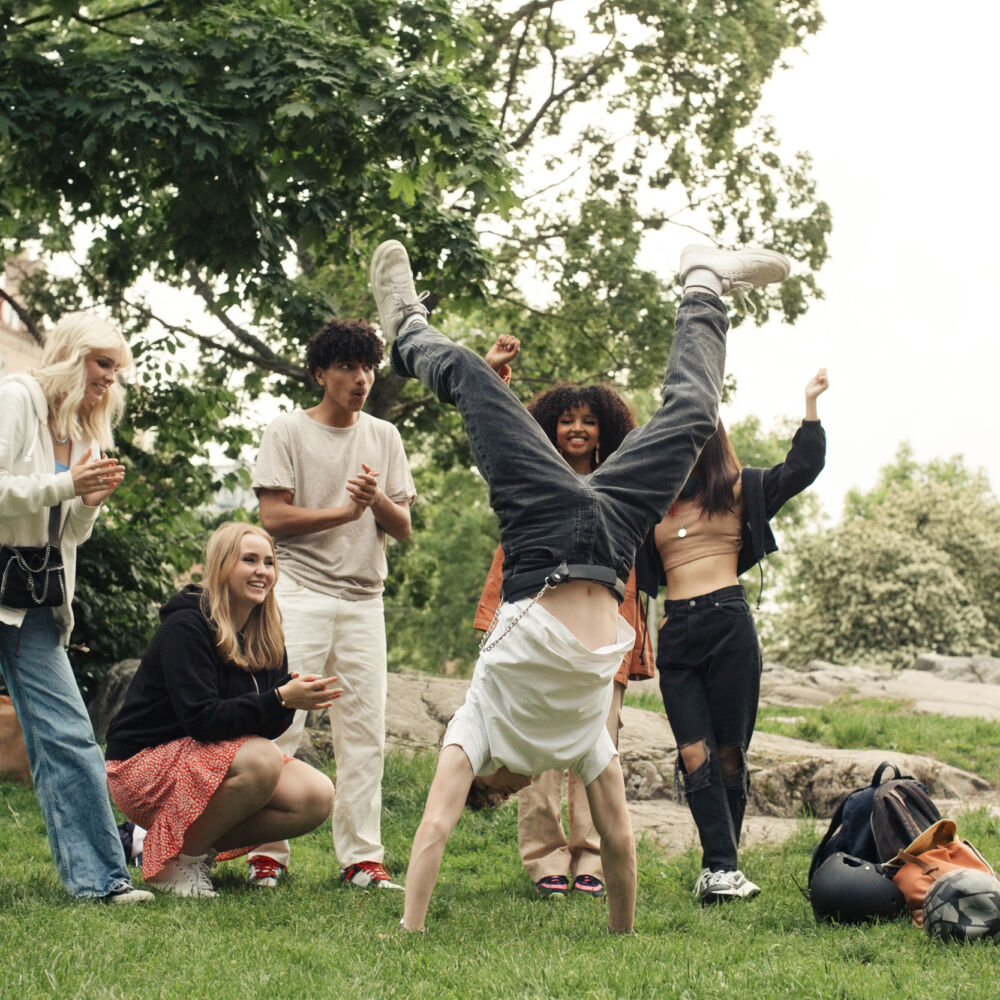 Kille står på händerna i park medan vänner hejar på